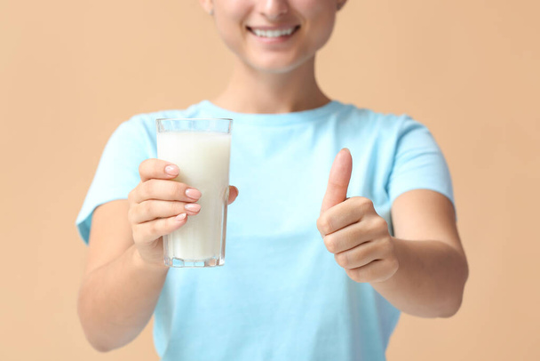 Mujer joven con vaso de leche orgánica mostrando gesto de pulgar hacia arriba en el fondo de color, primer plano - Foto, imagen