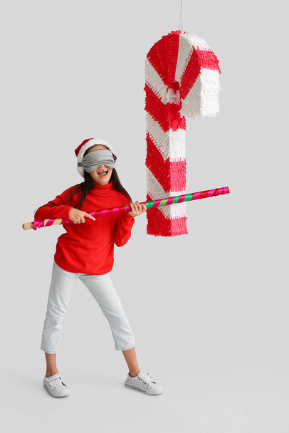 Klein meisje in Santa hoed en met snoep stok pinata op lichte achtergrond - Foto, afbeelding