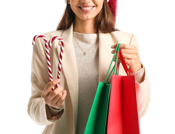 Beautiful woman with candy canes and shopping bags on white background - Photo, Image