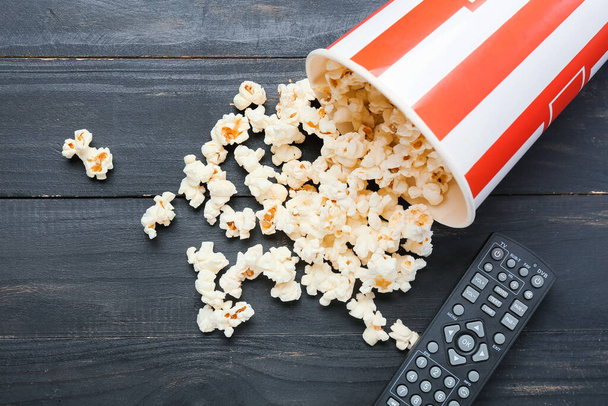 Moderne TV-Fernbedienung und Eimer mit Popcorn auf dunklem Holzgrund - Foto, Bild