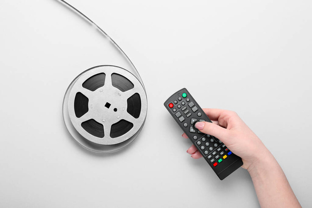 Frauenhand mit TV-Fernbedienung und Filmrolle auf grauem Hintergrund - Foto, Bild