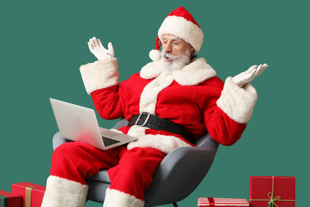 Sorprendido Santa Claus con portátil y regalos en el fondo de color - Foto, imagen