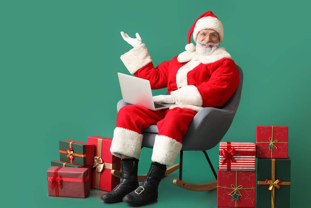 Kerstman met laptop en geschenken op kleur achtergrond - Foto, afbeelding