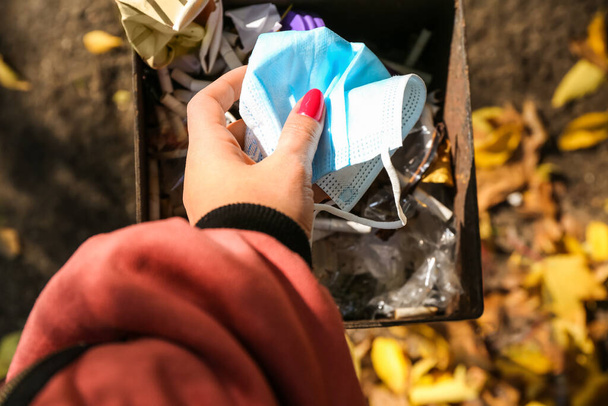 Woman throwing used medical mask in garbage bin outdoors - Φωτογραφία, εικόνα