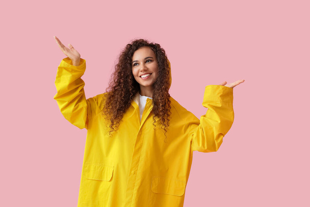 Young African-American woman in yellow raincoat on pink background - Foto, afbeelding
