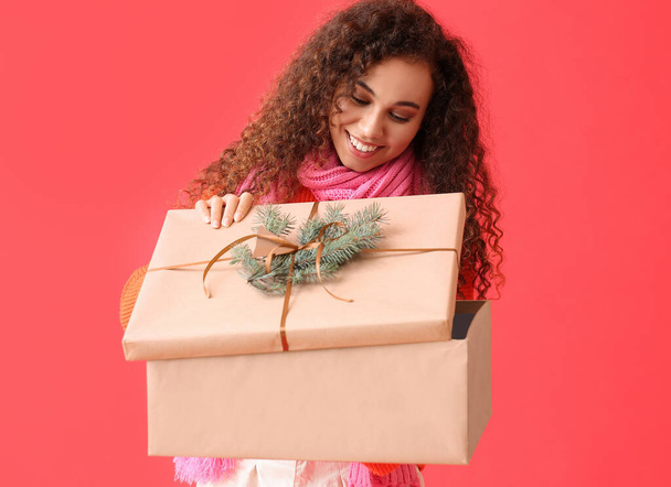 Jovem mulher afro-americana abrindo grande caixa de presente de Natal no fundo vermelho - Foto, Imagem