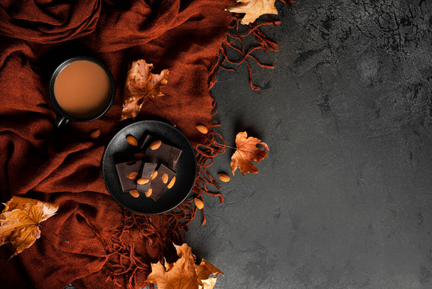 Composición de otoño. Bufanda marrón, café con leche, chocolate negro con almendras y hojas de arce de otoño. Acostado. Vista superior. - Foto, imagen