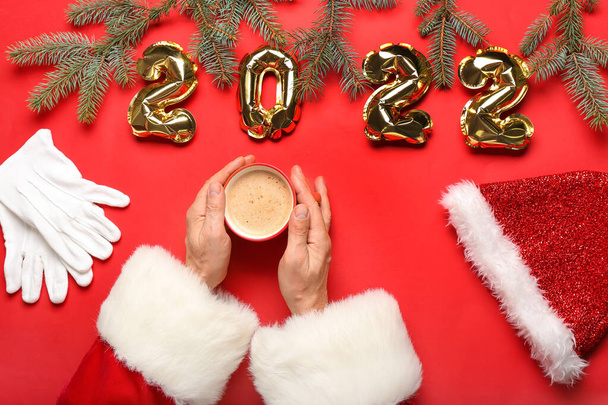 Santa Claus with cup of coffee and balloons in shape of figure 2022 on red background - Photo, Image