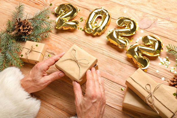 Άγιος Βασίλης με δώρο Χριστουγέννων και μπαλόνια σε σχήμα φιγούρα 2022 σε ξύλινο φόντο - Φωτογραφία, εικόνα