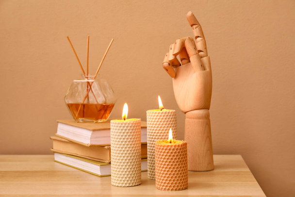 Velas ardientes, mano de madera, pila de libros y difusor de caña en mesa de madera cerca de la pared de color - Foto, imagen