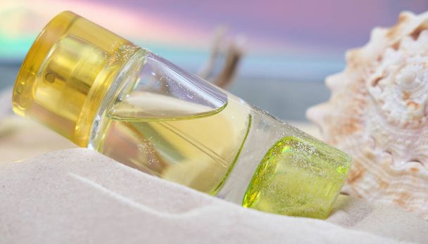 láhev jasně žlutého parfému na písečné pláži vedle mušle. lehké a vzdušné letní vůně pro ženy. vůně pro dovolenou. - Fotografie, Obrázek