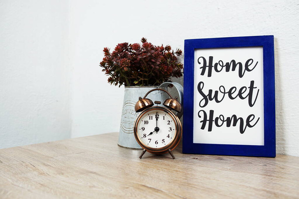 Home Sweet Home typography text and alarm clock on wooden table and white wall background - Foto, immagini
