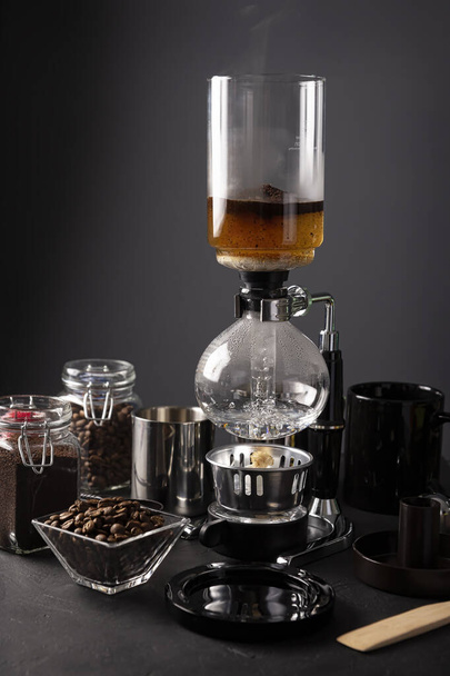 Vacuum coffee maker also known as vac pot, siphon or syphon coffee maker and toasted coffee beans on rustic black stone table. - Foto, afbeelding