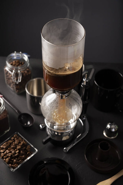 Vacuum coffee maker also known as vac pot, siphon or syphon coffee maker and toasted coffee beans on rustic black stone table. - Foto, Imagem