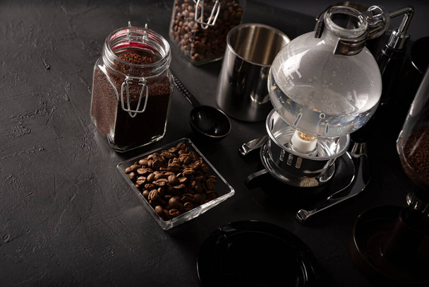 Vacuum coffee maker also known as vac pot, siphon or syphon coffee maker and toasted coffee beans on rustic black stone table. Copy space for your text - Foto, Bild