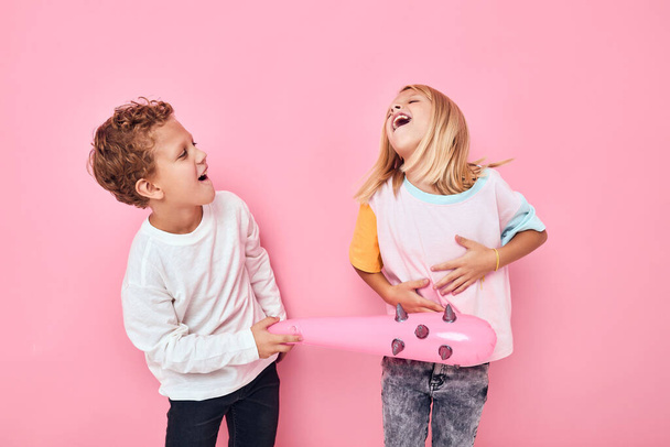 Vrolijke jongen en meisje speelgoed op roze achtergrond. Hoge kwaliteit foto - Foto, afbeelding