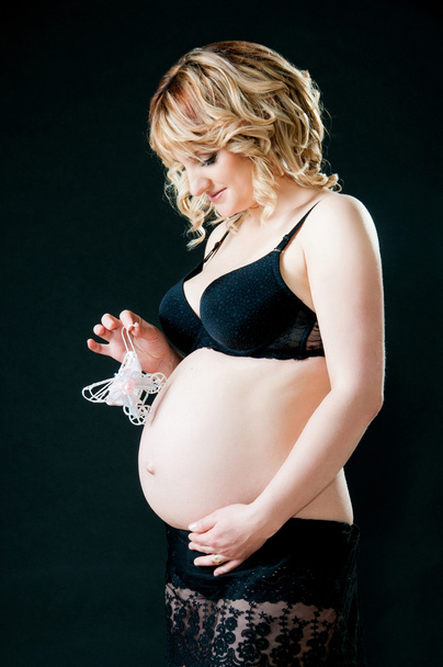 Pregnant woman on a black background holding a baby pram near tummy. - Fotoğraf, Görsel