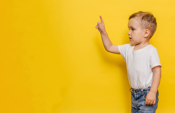 A little boy on a yellow background points to the background. Copy space. - Photo, image