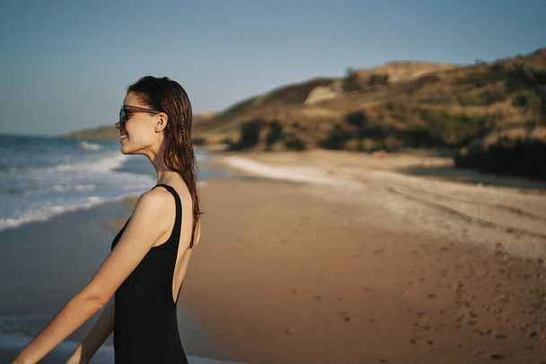 woman walks along the sandy shore in a black swimsuit sun tropics - Fotó, kép