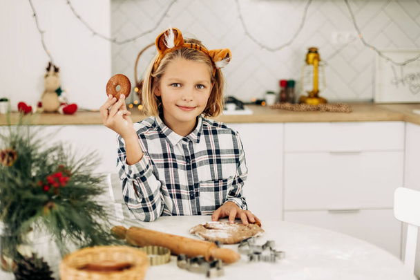 Porträt eines fröhlichen Mädchens, das ein weihnachtliches Deko-Plätzchen in der Hand hält. Vorbereitung auf die Feiertage, Weihnachtsstimmung, weihnachtliche Leckereien - Foto, Bild