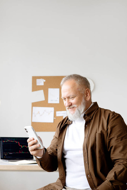 an elderly man works in a stock market through the phone. In a bright office - Foto, afbeelding