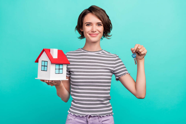 Photo of optimistic millennial brunette lady sell house wear striped t-shirt isolated on teal color background. - 写真・画像