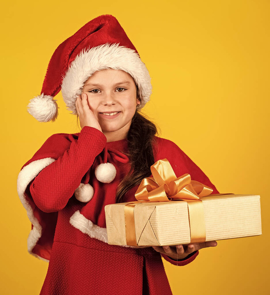 Dreams come true. Winter holidays. My happy day. Xmas gift shopping. Gift package. Small girl Santa hat hold gift box. Kid hold present box yellow background. Merry Christmas and happy holidays - Foto, imagen