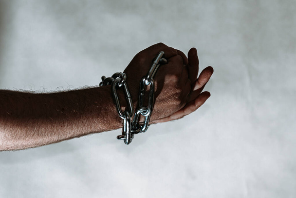 Men 's hand in a steel chain.Steel chains in the hands of man on a gray wall background.Toned.Tonseup, selective focus.Copy space. - Фото, изображение