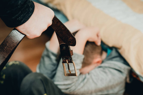 Concept de violence familiale et d'agression - l'homme furieux a levé le poing de punition avec la ceinture sur l'enfant effrayé à la maison.. - Photo, image