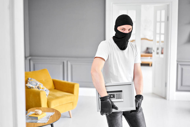 Thief with black mask stealing modern Metal safe with an electronic lock. Home theft of money and documents concept. - Zdjęcie, obraz