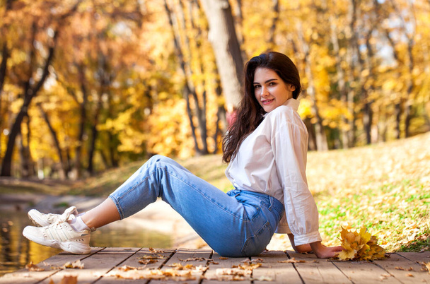 Full-length portrait of a young girl in blue jeans posing in an autumn park - Foto, afbeelding