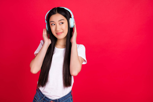 Photo of curious flirty lady enjoy music look empty space wear earphones white t-shirt isolated red color background. - 写真・画像