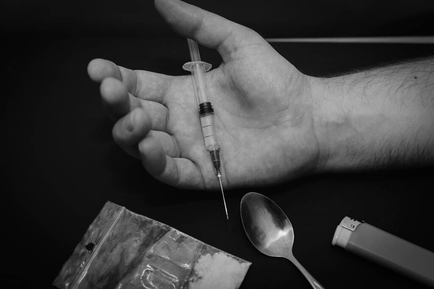 Main toxicomane avec seringue sur chambre noire avec un sac de drogue une cuillère et un briquet.. - Photo, image