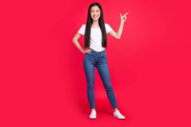 Photo of chinese lady indicate finger empty space wear white t-shirt jeans shoes isolated red color background. - Foto, imagen