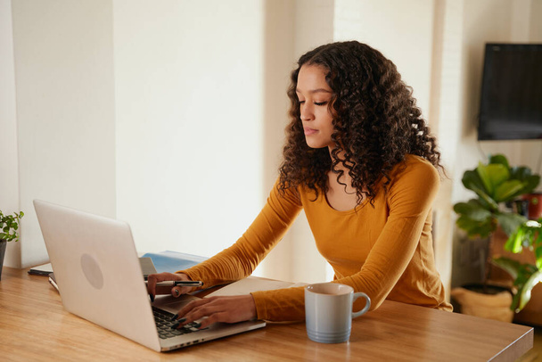 Çok kültürlü bir kadın evde çalışırken odaklanıyor. Modern dairede dizüstü bilgisayarda genç profesyonel daktilo. - Fotoğraf, Görsel