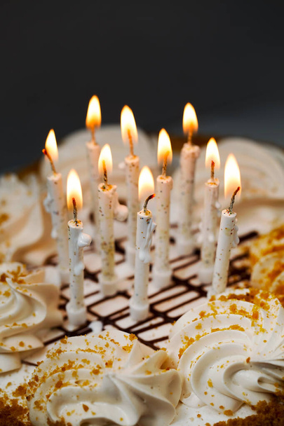 Burning candles on a honey cake. Beautiful white candles burn brightly. Traditional birthday cake. Vertical image - Фото, изображение