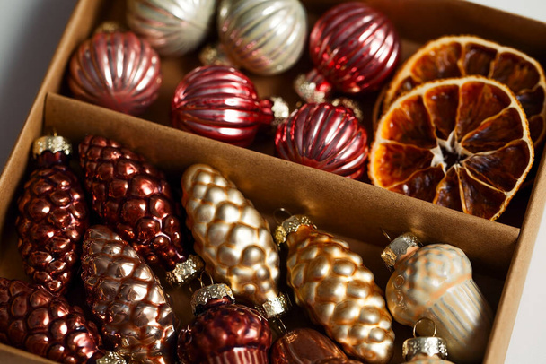 Vintage glass cones, balls and acorns. Dried slices of oranges and tangerines. Golden and brown Christmas decor in a cardboard box. - Photo, Image