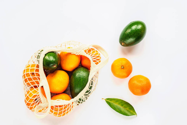 Tangerines en avocado in een touwentas. Geen afval concept. Gezond eten, rauw veganistisch. Bovenaanzicht, platte lay, witte achtergrond. - Foto, afbeelding