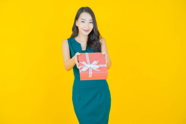 Портрет красива молода азіатка посміхається з червоною подарунковою коробкою на кольоровому фоні
 - Фото, зображення
