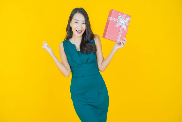 Portrét krásná mladá asijská žena úsměv s červeným dárkem box na barevném pozadí - Fotografie, Obrázek