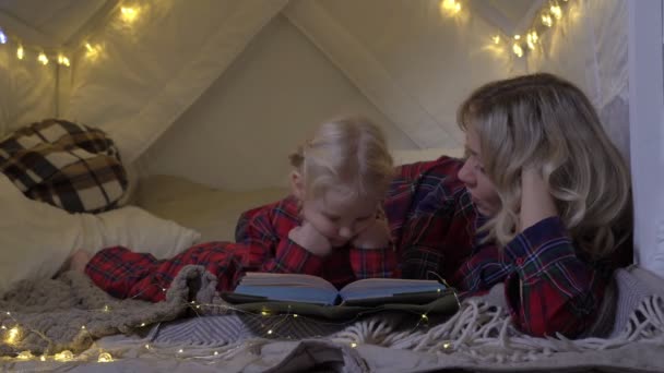Mom reads a book to her daughter before bedtime. A woman reads a fairy tale to a child before Christmas - Footage, Video