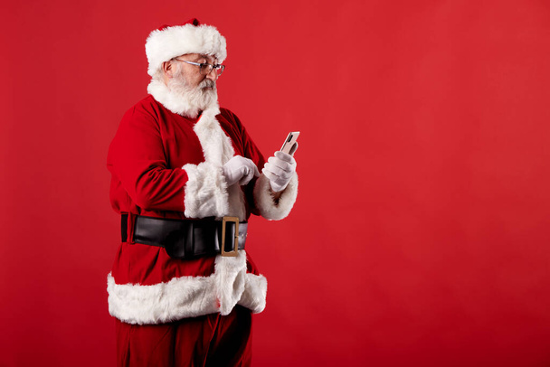 Άγιος Βασίλης χρησιμοποιώντας ένα κινητό τηλέφωνο σε κόκκινο φόντο - Φωτογραφία, εικόνα