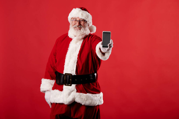 Santa Claus usando un teléfono móvil sobre fondo rojo - Foto, Imagen