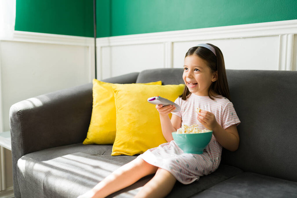 Nadšené dítě hledá film sledovat v televizi a smát se při relaxaci a těší popcorn v obývacím pokoji  - Fotografie, Obrázek