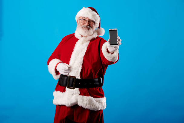 Санта-Клаус с помощью мобильного телефона на синем фоне - Фото, изображение