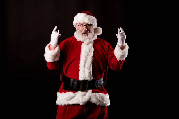 Санта Клаус делает рокерский жест на черном фоне - Фото, изображение