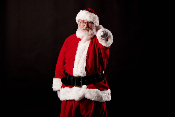 Der Weihnachtsmann zeigt mit dem Finger in die Kamera auf schwarzem Hintergrund - Foto, Bild