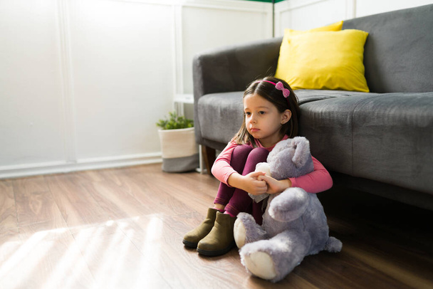 Грустный одинокий ребенок. Красивая маленькая девочка обнимает плюшевого мишку, скучая по маме и папе - Фото, изображение