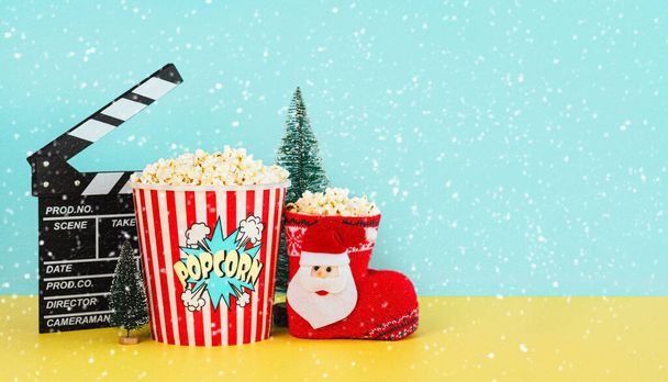 黄色と青の背景にテキストのためのポップコーン、クリスマスの装飾、雪の結晶とスペースと映画のクラッパーボード。クリスマス映画のコンセプト - 写真・画像
