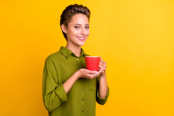 Photo of positive nice glad lady hold mug drink tea shiny smile wear green shirt isolated yellow color background. - Photo, Image
